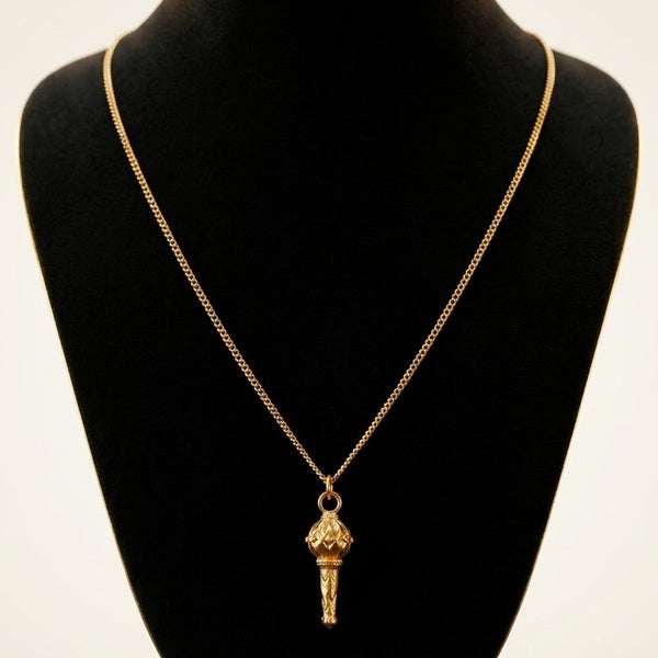 A gold pendant necklace featuring a detailed, textured flame-shaped charm, displayed on a black velvet jewelry bust against a light background.