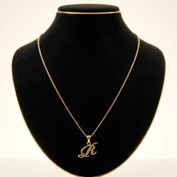 A gold initial necklace featuring a cursive script letter 'R' pendant, displayed on a black velvet jewelry bust against a light background.